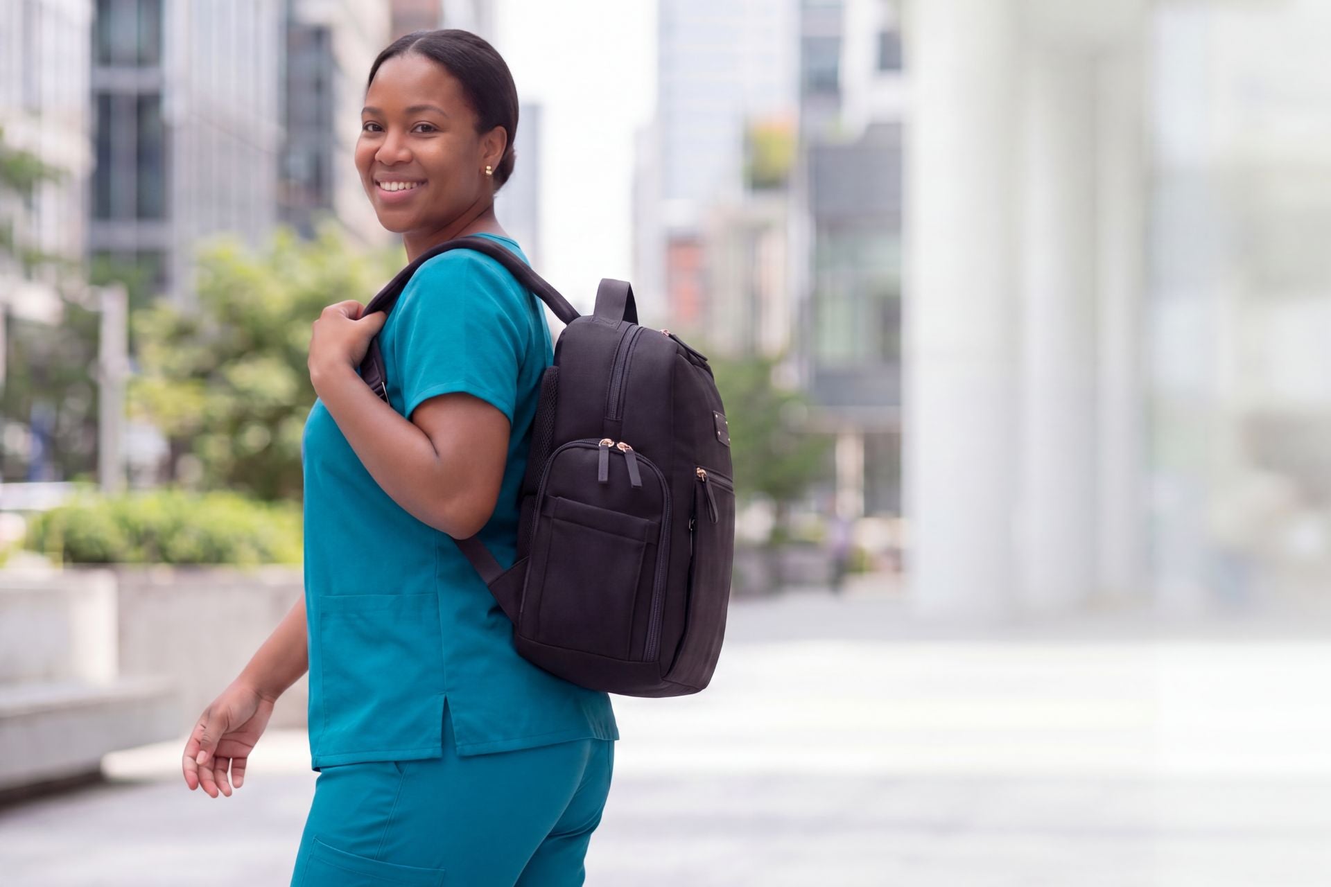 Healthcare worker in teal scrubs wearing a black Fiona breast pump backpack by Sarah Wells